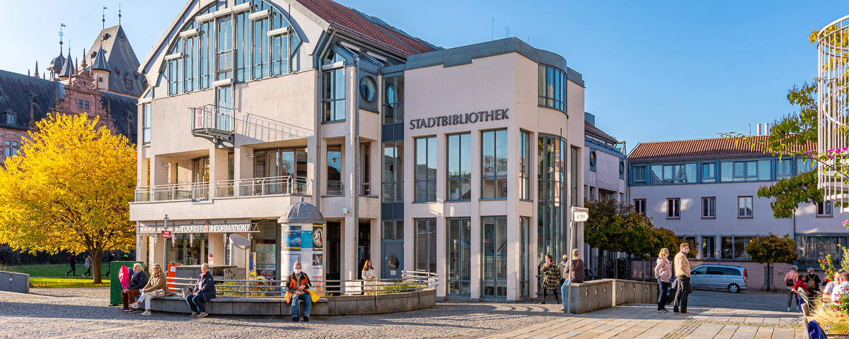 Außenaufnahme der Stadtbibliothek vom Marktplatz aus im Herbst mit einem gelben Laubbaum links von der Bibliothek