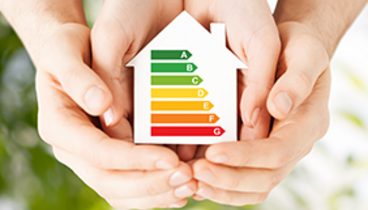 Dekoratives Bild, Hände umschließen eine Haus, auf dem eine Energieskala zu sehen ist.