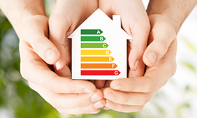 Dekoratives Bild, Hände umschließen eine Haus, auf dem eine Energieskala zu sehen ist.