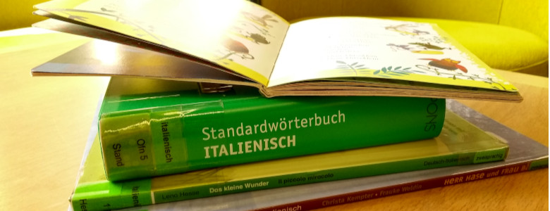 Übereinandergestapelte Bücher auf einem Tisch, dazwischen ein italienisches Wörterbuch