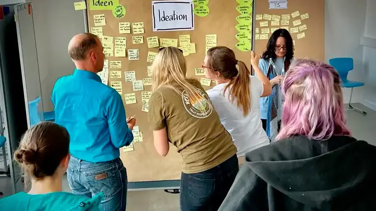 Mehrere Teilnehmende betrachten eine Wand mit Post-Its.