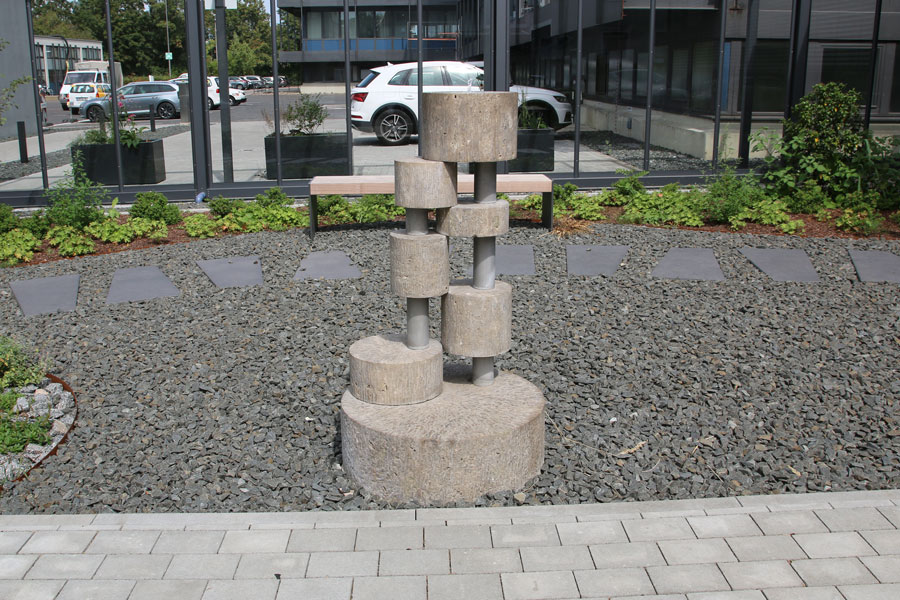 Trinkwasserbrunnen, auf Steinen, vor Glaswand