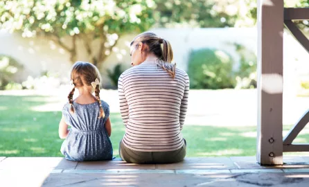 Auf dem Bild ist eine Frau mit einem kleinen Kind zu sehen. Aufgenommen sitzend von hinten Fotografiert auf einer Veranda.