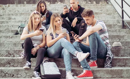 Auf dem Bild ist eine Gruppe Jugendlicher auf einer Treppe sitzend zu sehen mit Smartphone in der Hand.