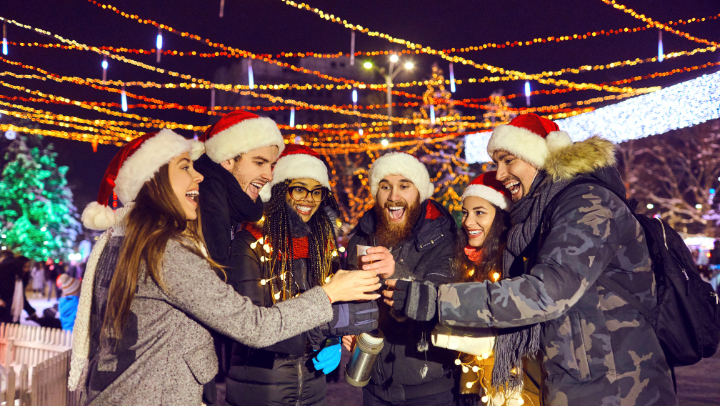 Sechs Freunde (drei Männer, drei Frauen, die auf dem Weihnachtsmarkt miteinander anstoßen.