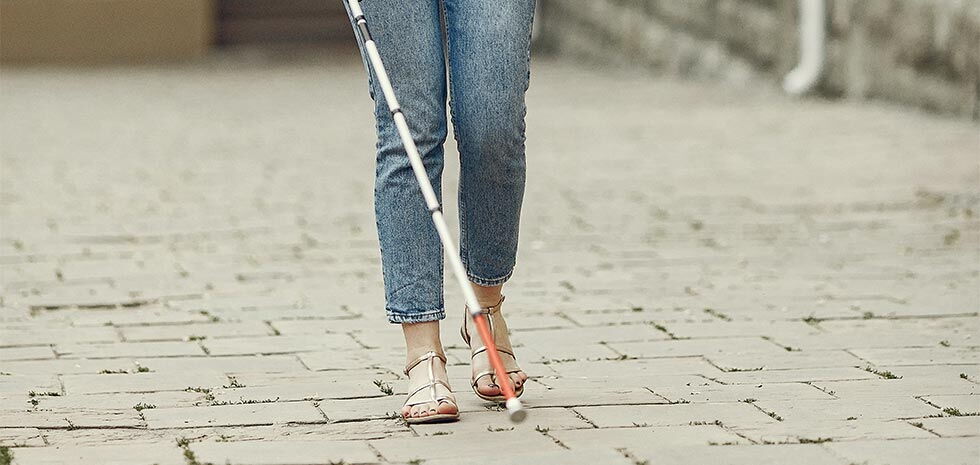 Nahaufnahme einer Person mit Blindenstock auf einem Pflasterweg – Symbol für Barrierefreiheit und Inklusion.